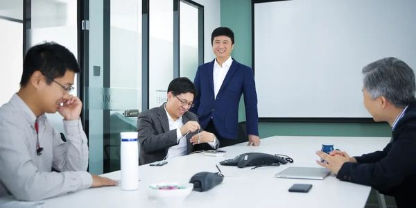 Four men in a modern office having a casual meeting around a white table.